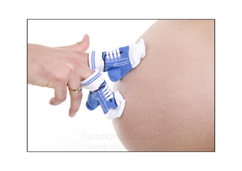 Fotografia ciążowa, małe niebieskie buciki na brzuszku kobiety w ciąży