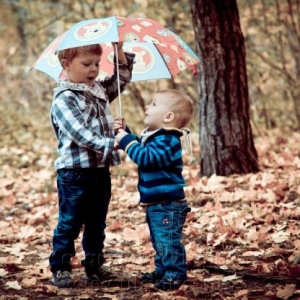 Dwaj chłopcy pod parasolką wśród liści