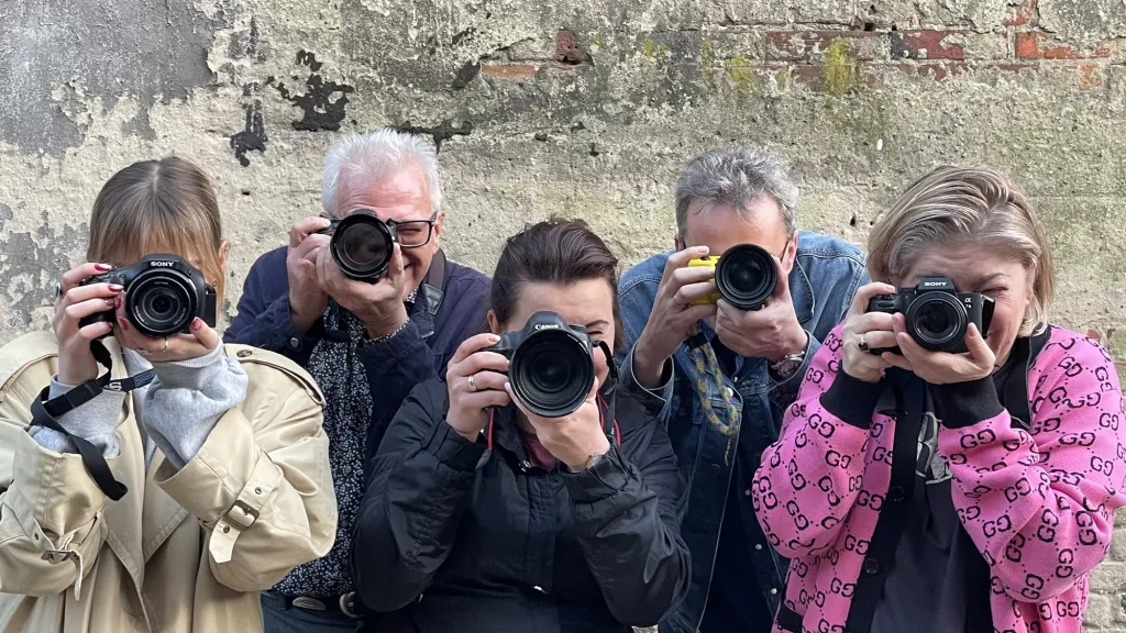Uczestnicy warsztatów fotograficznych z aparatami przy ceglanym murze