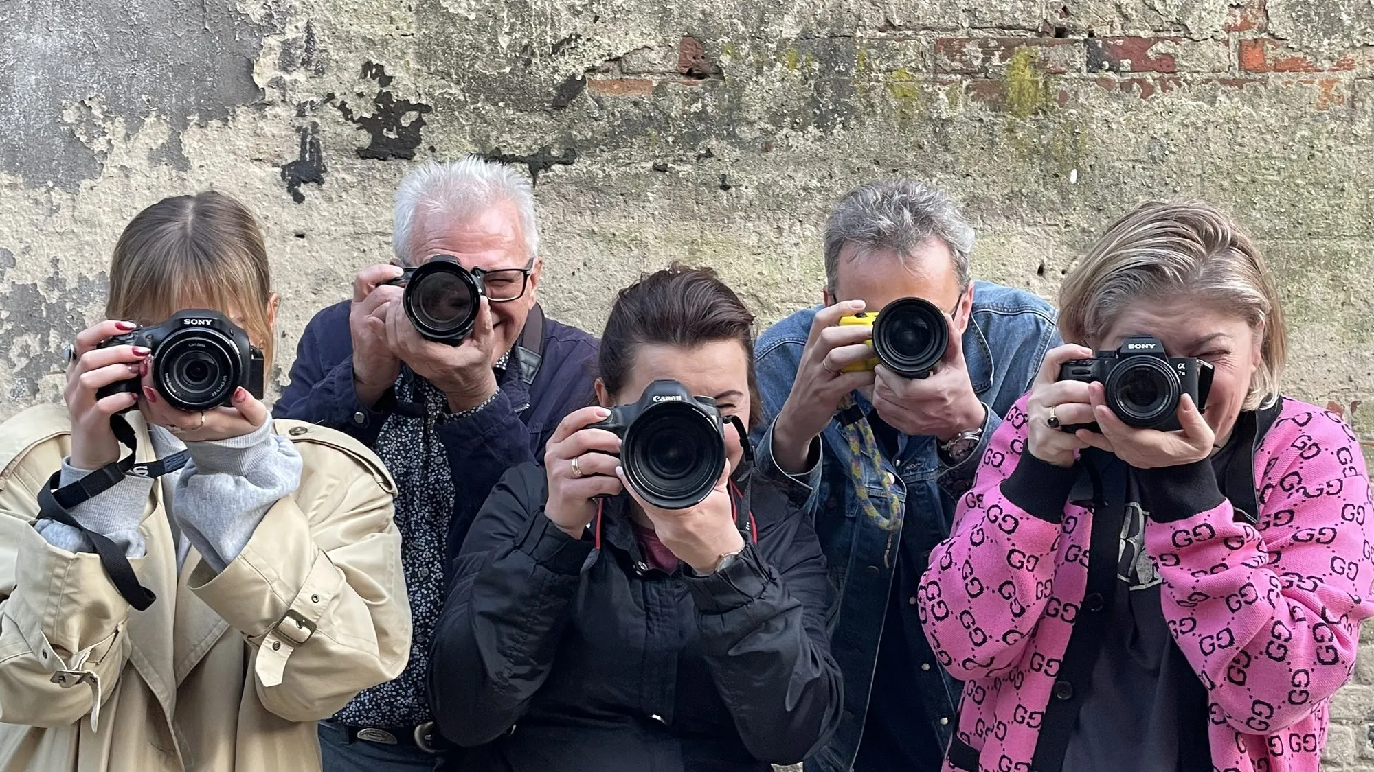Uczestnicy warsztatów fotograficznych z aparatami przy ceglanym murze